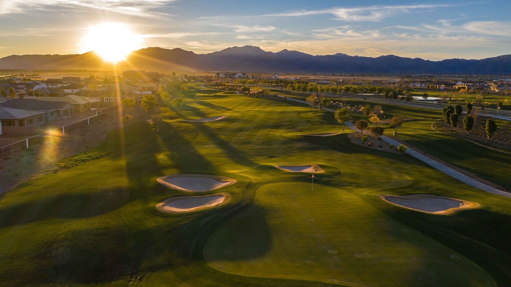 A golf course with bunkers and a sunset in the background.