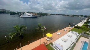 Un hotel sul lungomare con piscina, lettini e vista su un grande yacht.