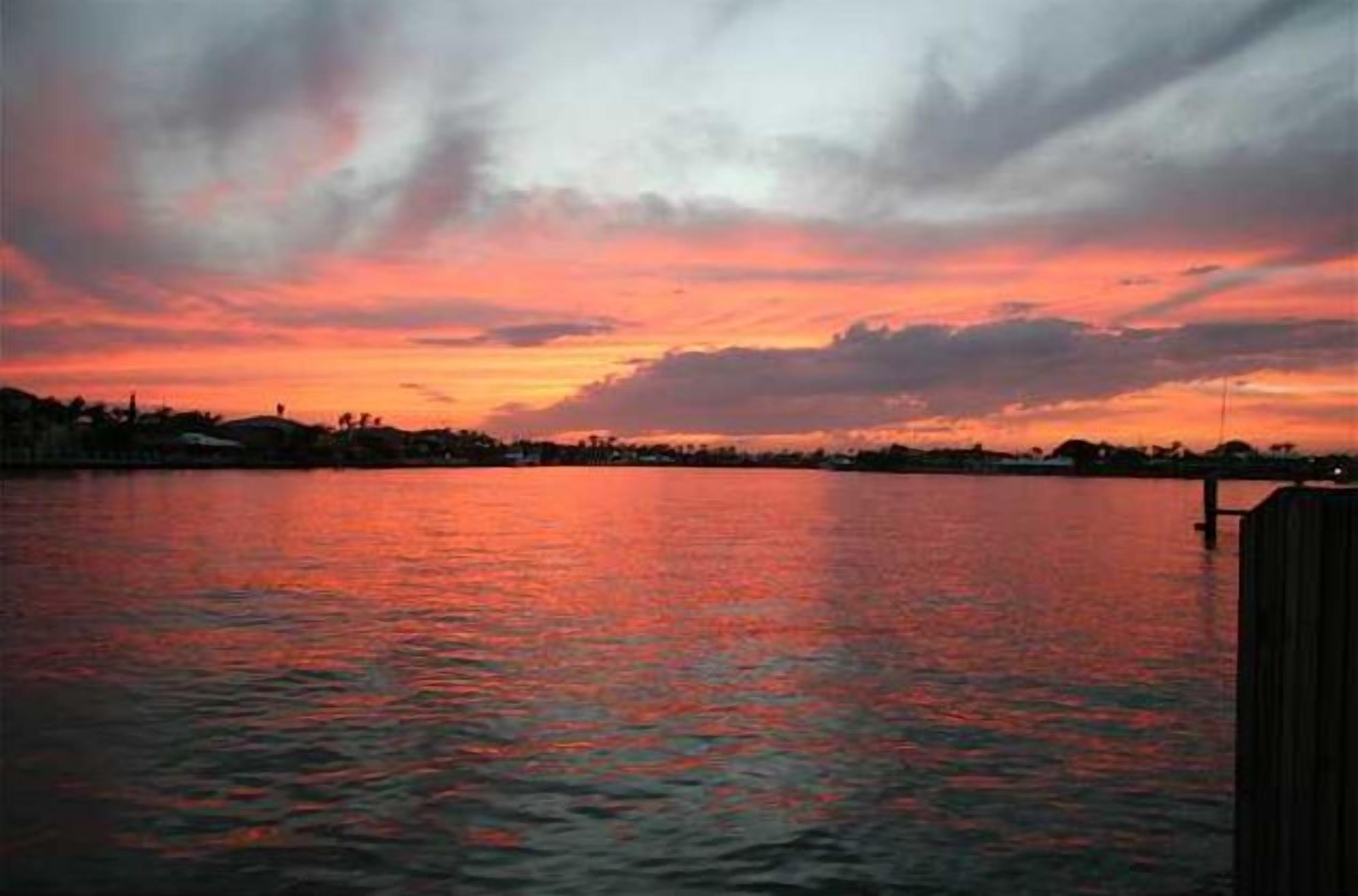 Un coucher de soleil sur une étendue d’eau calme, avec un quai sur la droite.