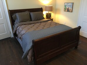 Un lit en bois recouvert d’une courtepointe, une lampe de chevet et un tableau accroché au mur.