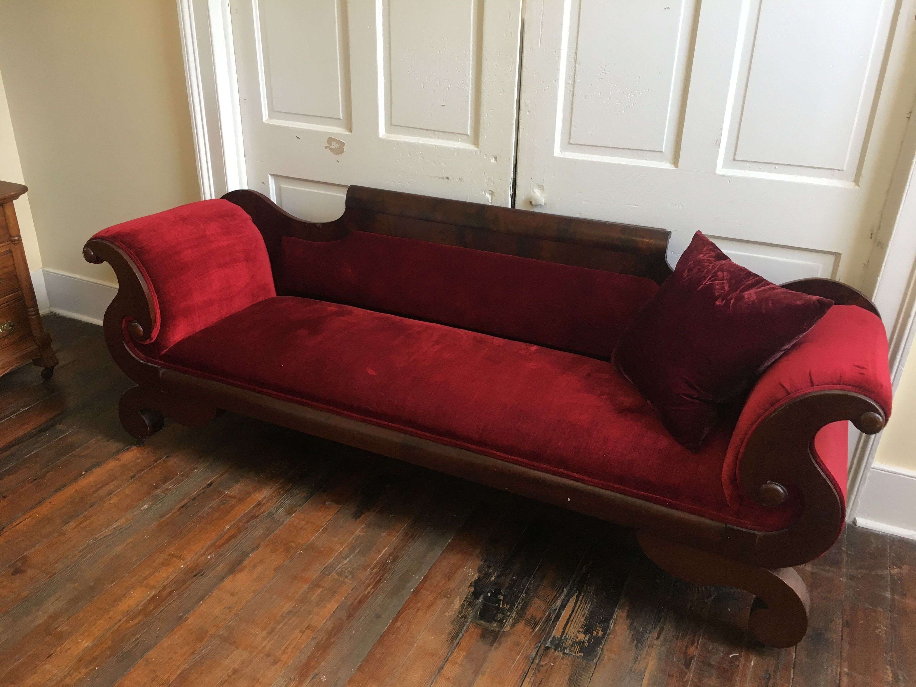 Un divano in velluto rosso con schienale e braccioli curvi, posto di fronte a una porta bianca con pannelli.