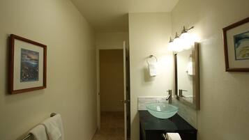 A bathroom with a glass sink, a towel rack, a framed picture on the wall, and a door leading to another room.