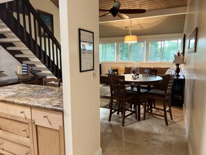 A kitchen with a granite countertop, wooden cabinets, a dining area with a round table and chairs, a ceiling fan, and a large window with a view of greenery outside. - Turtle Bay Condo: Hawaiian Style & Cozy! Permit: 2211-CCH-0078 (Kahuku)