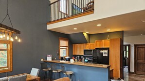 A modern kitchen with a bar area, wooden cabinets, and a dining space with a sofa and chairs.