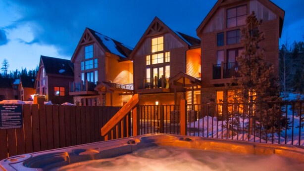A wooden lodge with multiple buildings, a hot tub, and a wooden fence.