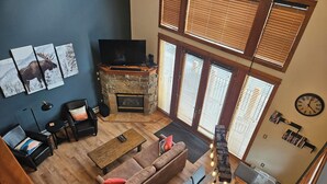 A spacious living room with a stone fireplace, a large flat-screen TV, and a cozy seating area with a brown sofa and armchairs.