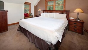 A bedroom with a large bed, two bedside tables with lamps, a wooden headboard, and a window with a view of trees.