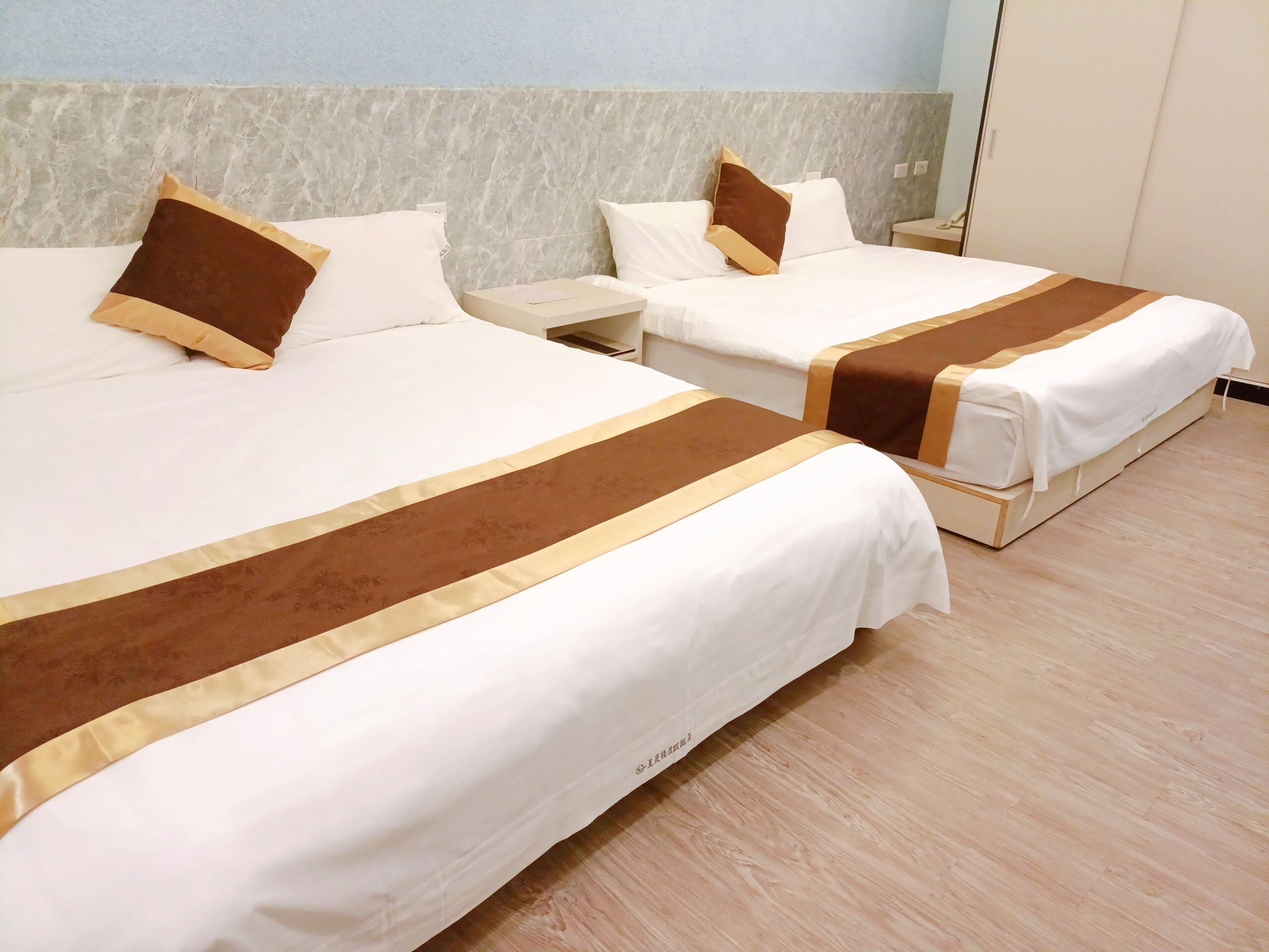 Una habitación de hotel con dos camas, cada una con ropa de cama blanca y detalles en tonos marrones.