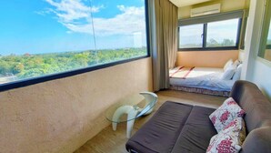 A room with a bed, a sofa, a small table, and a large window offering a view of greenery. - Starry Inn (Xincheng)