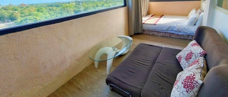Una habitación con una cama, un sofá, una mesita y un ventanal grande que ofrece vistas a zonas verdes.