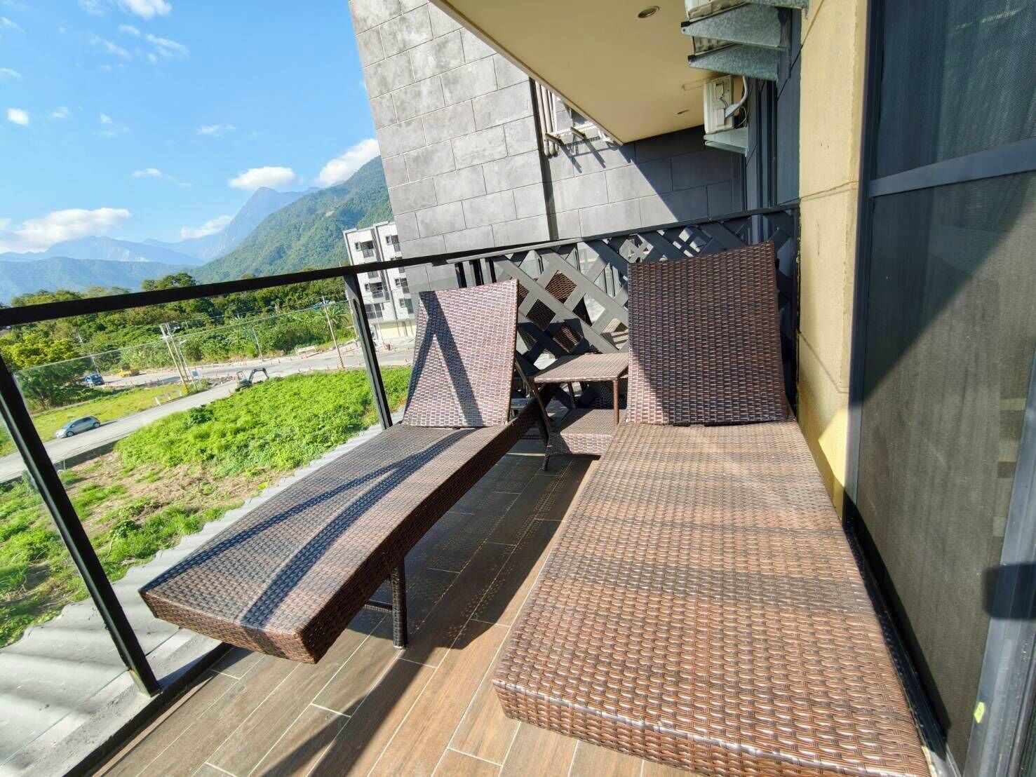 A balcony with wicker furniture, a view of a road, and mountains in the background.
