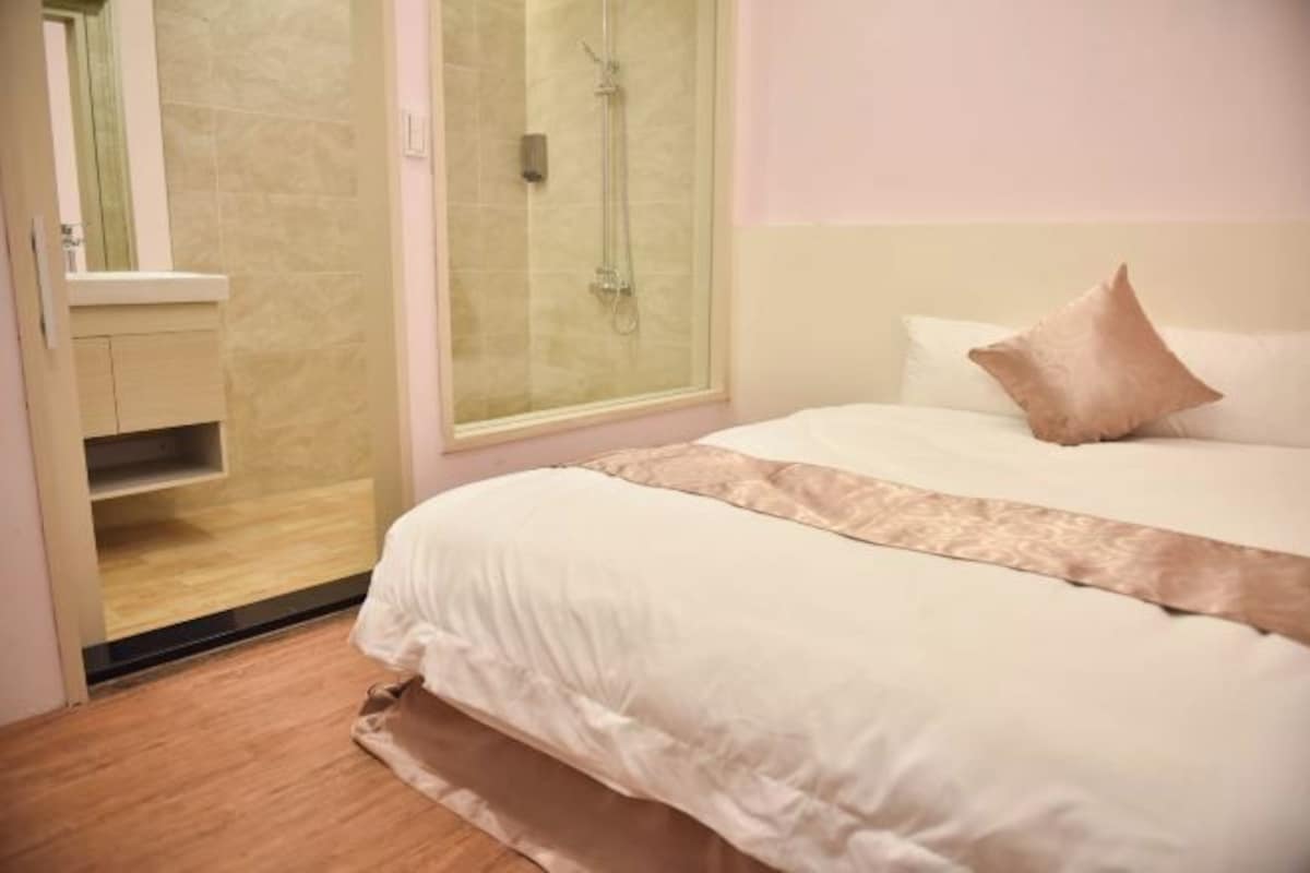 A bedroom with a bed, a window, a shower, and a vanity.