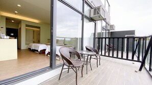 A balcony with wicker chairs and a glass table, overlooking a bedroom with a bed and a desk. - Starry Inn (Xincheng)