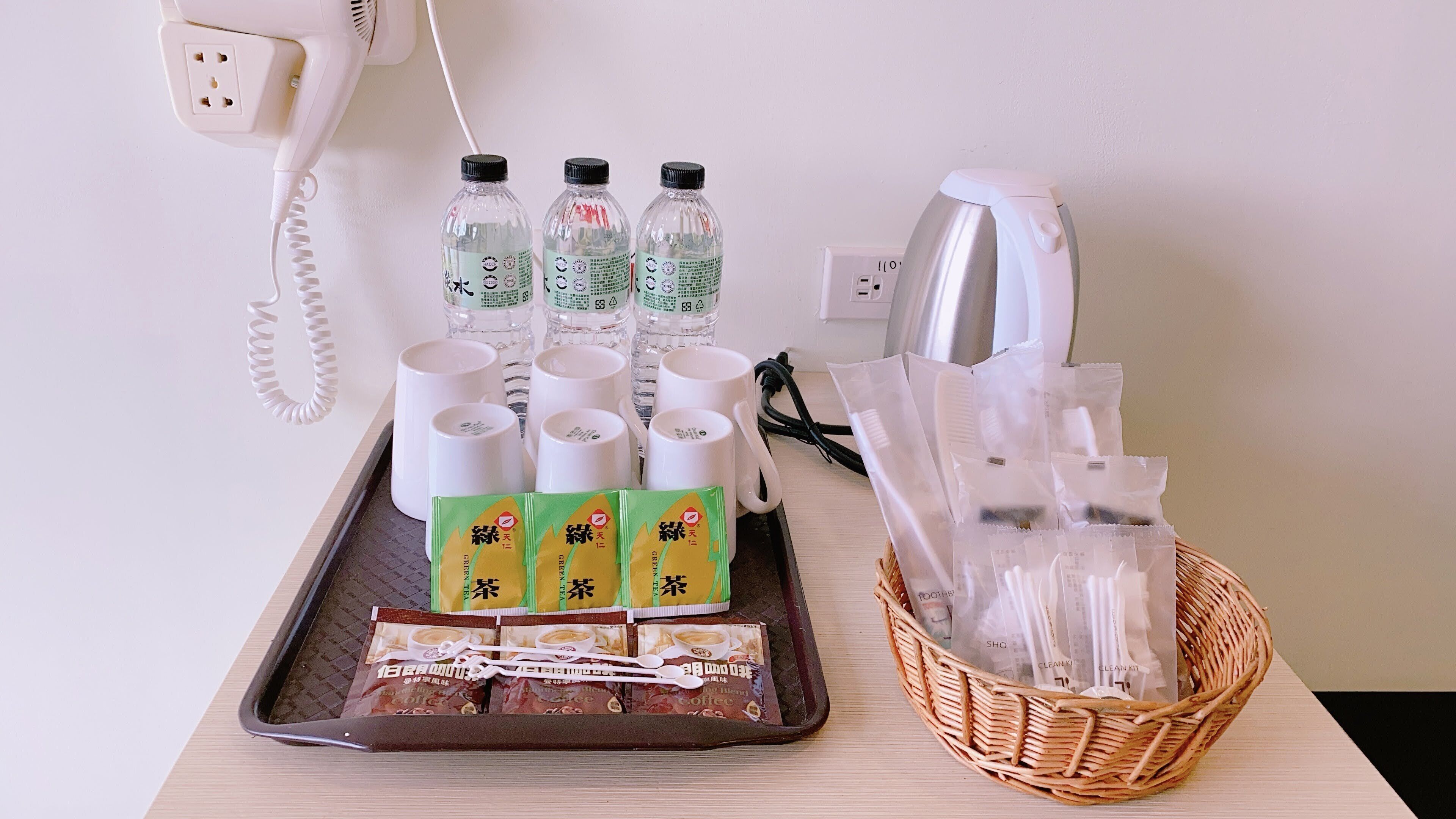 Una bandeja con sobres de café, botellas de agua y tazas blancas sobre una mesa.