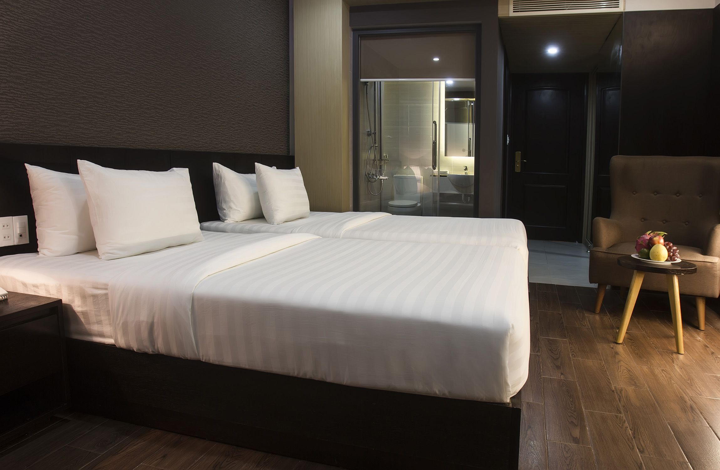 A modern hotel room with a large bed, a separate bathroom, and a small seating area with fruit.