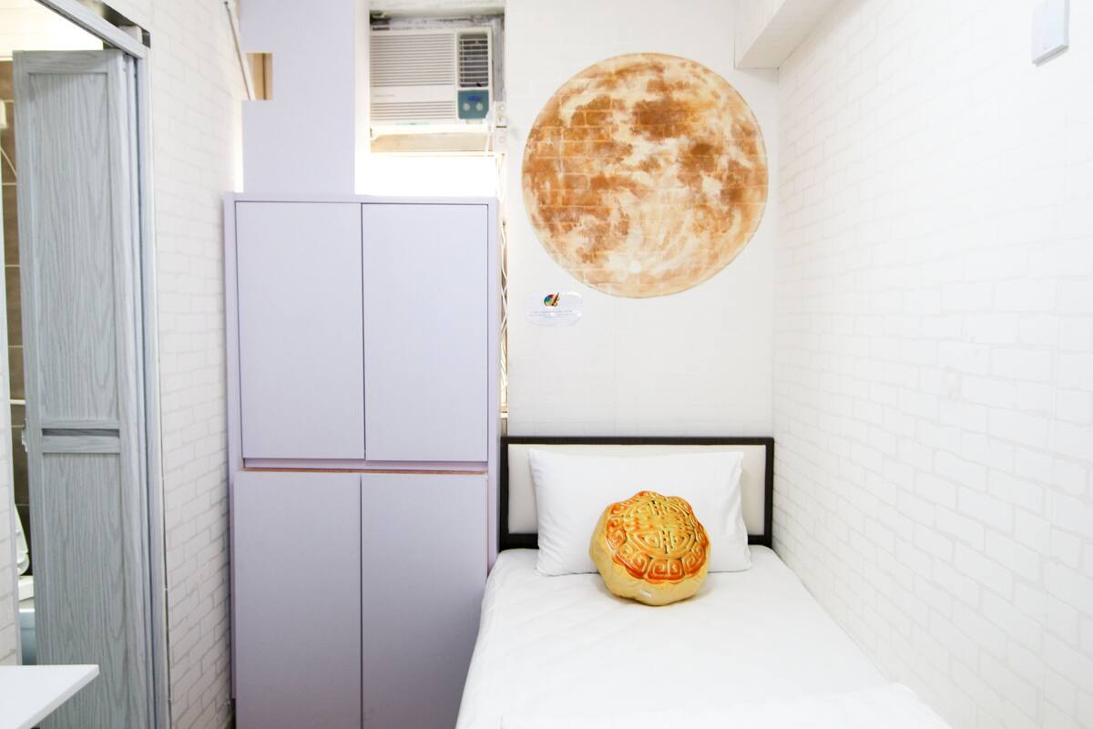 A bedroom with a bed, a wall-mounted air conditioner, and a large moon mural.