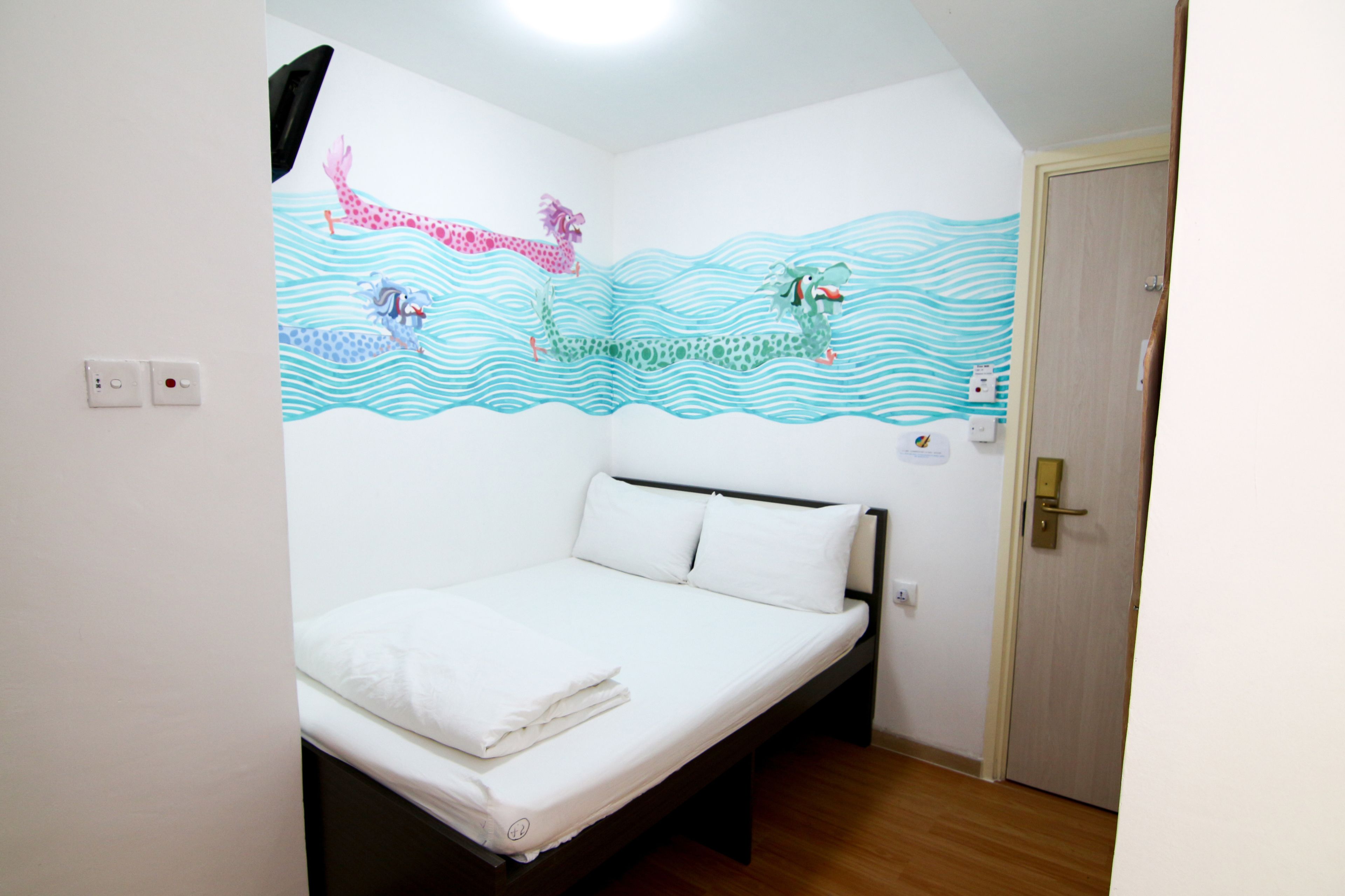A single-bed room with a white mattress, a wooden headboard, and a wall mural depicting a giraffe and a crocodile swimming.
