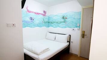 A single-bed room with a white mattress, a wooden headboard, and a wall mural depicting a giraffe and a crocodile swimming.