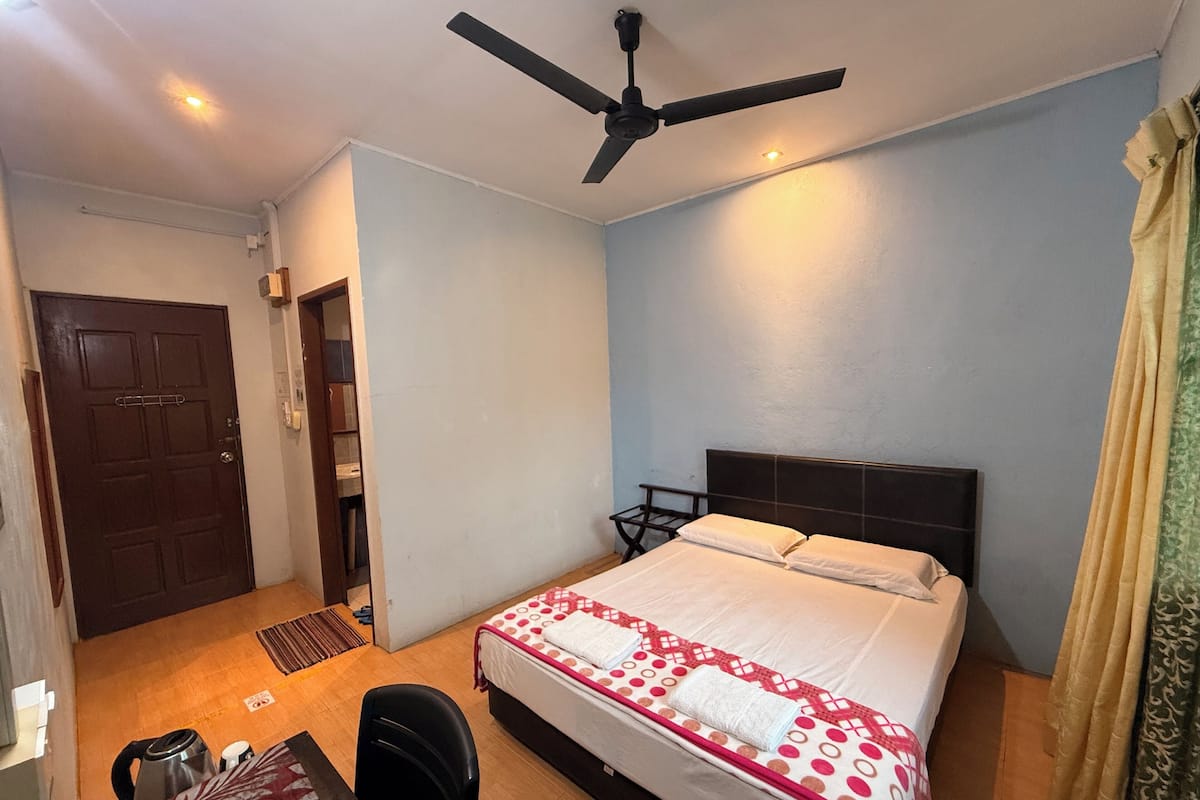 A bedroom with a bed, a ceiling fan, a desk, and a chair.