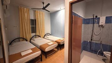 A room with two single beds, a ceiling fan, a window with curtains, and a bathroom with a shower and toilet.