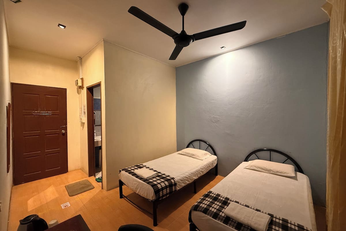 A room with two single beds, a ceiling fan, a door, and a small table.