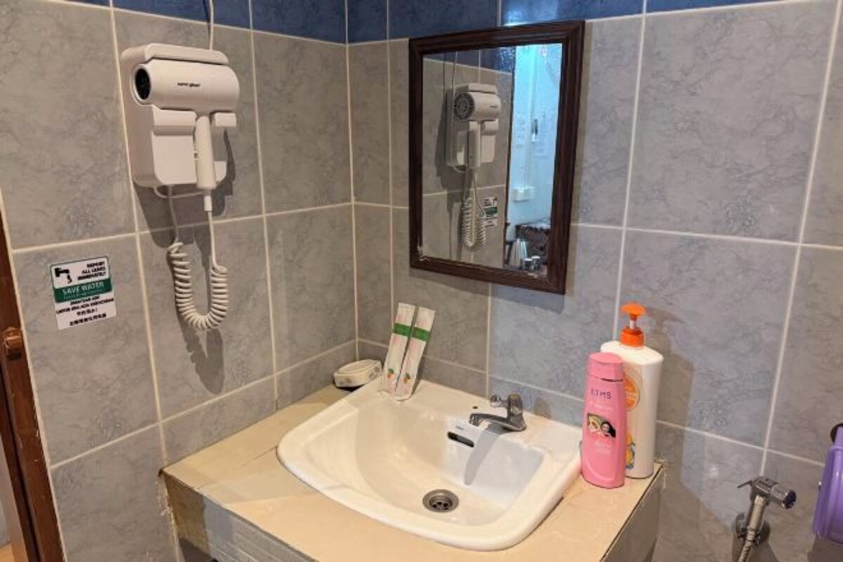 A bathroom with a sink, a hairdryer, a mirror, and toiletries on the counter.