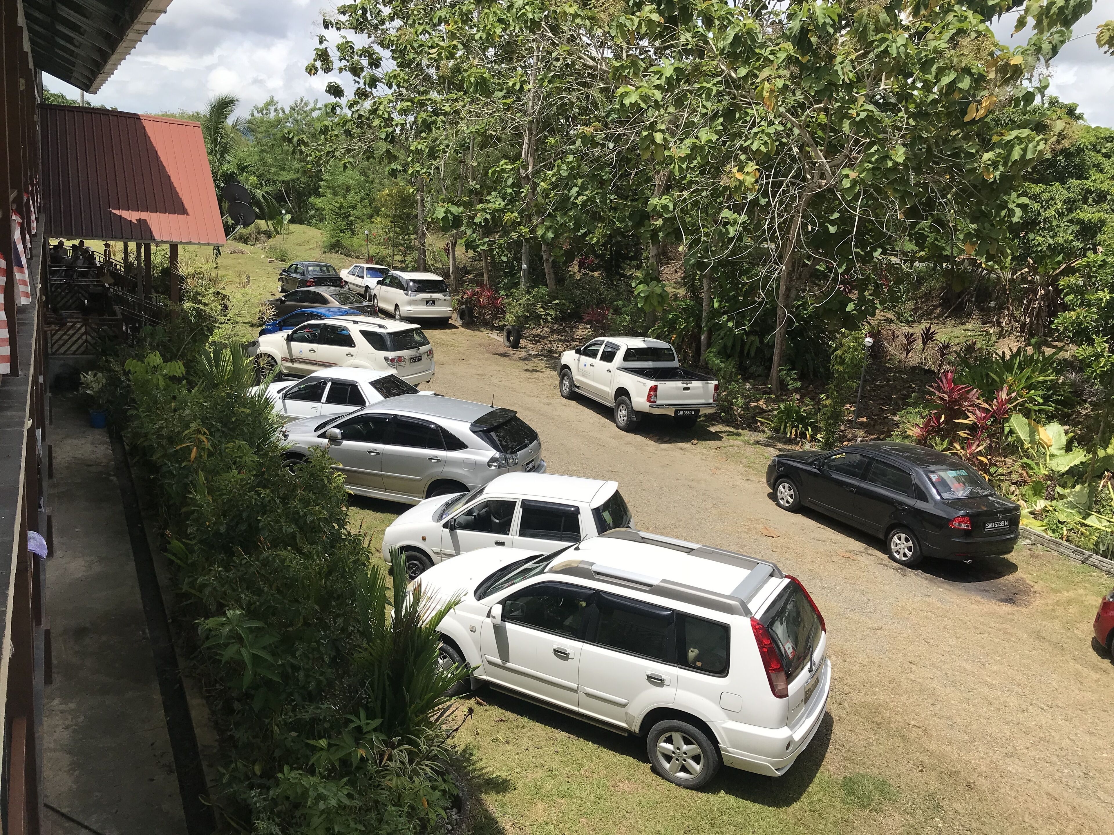 A parking area with multiple vehicles, surrounded by greenery and trees.