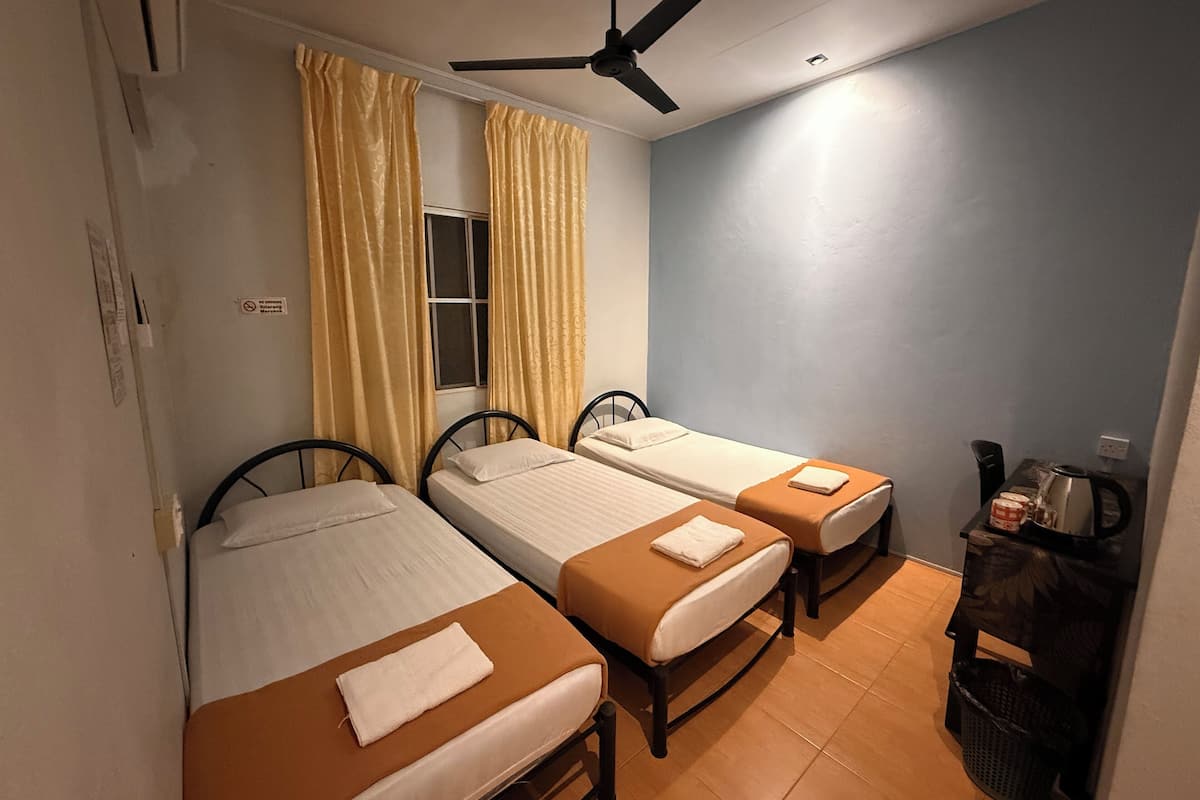 A room with two single beds, a ceiling fan, a window with yellow curtains, and a small table with a kettle and a mug.
