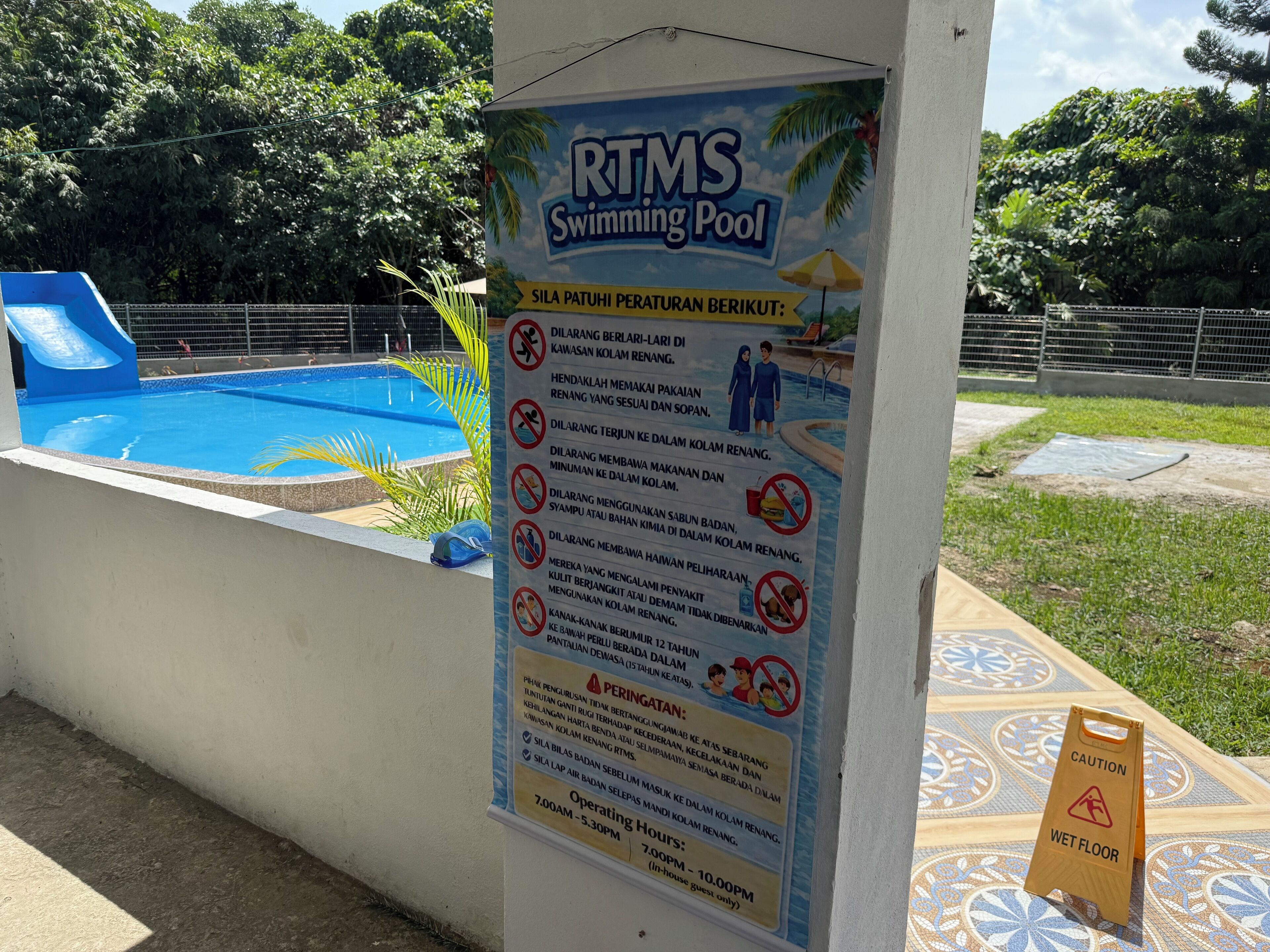 A swimming pool area with a sign listing rules and operating hours.