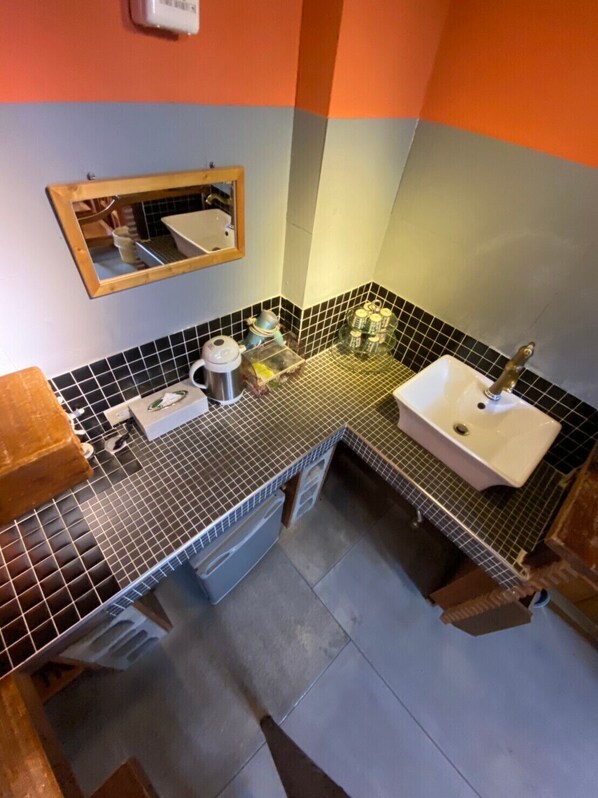 A bathroom with a tiled backsplash, a sink, a mirror, and a countertop with various items. - Good Harvest B&B (Chishang)