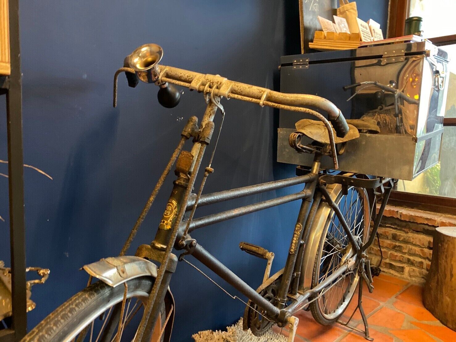 An antique bicycle with a wooden frame and metal components, leaning against a wall in a room with a blue wall and a tiled floor.