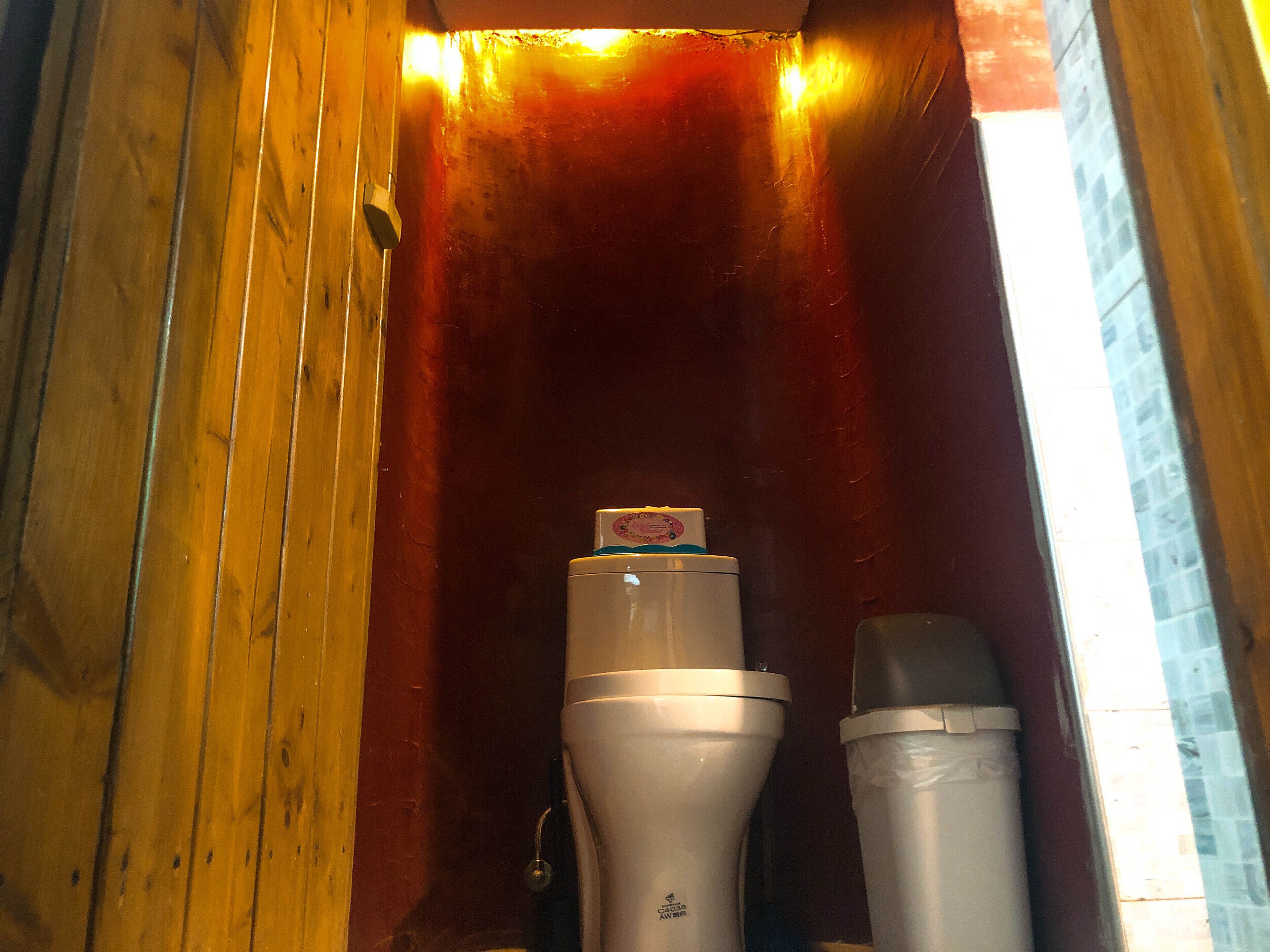 Un intérieur en bois avec un rideau rouge, des toilettes blanches et une poubelle.