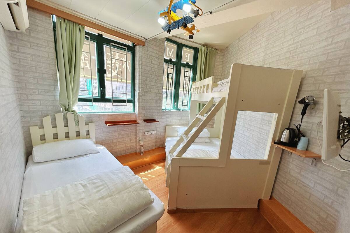 A compact room with two single beds, a bunk bed, a desk, and a chair.