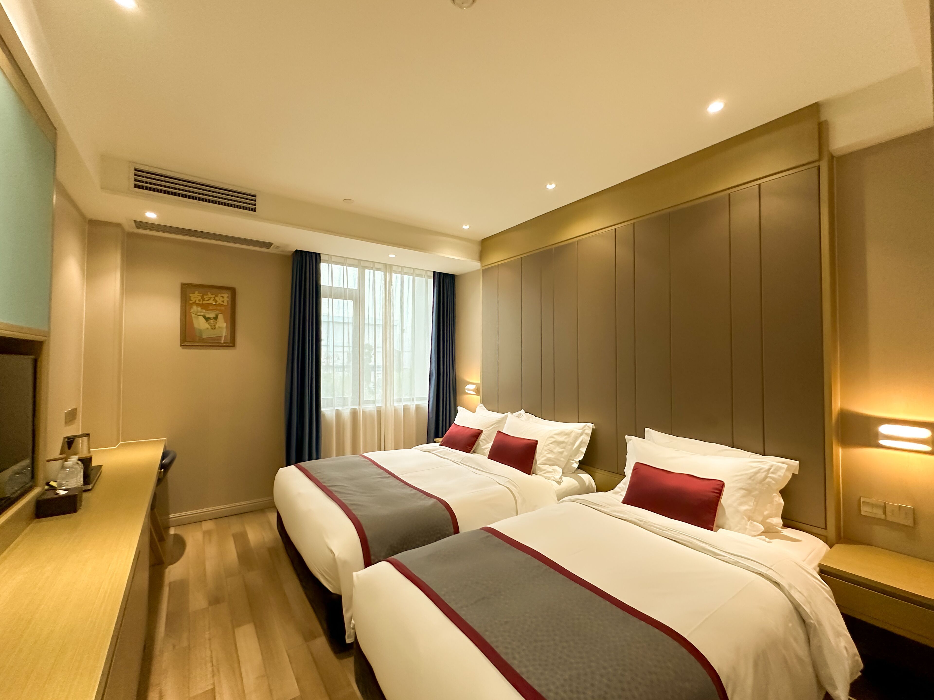 A hotel room with two beds, a desk, a chair, a TV, and a window with curtains.