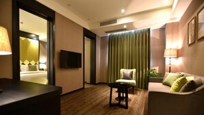 A hotel room with a wooden floor, a sofa, a chair, a TV, and a bed with a green curtain. - SHANGHAI-DECO Hotel (Shanghai)