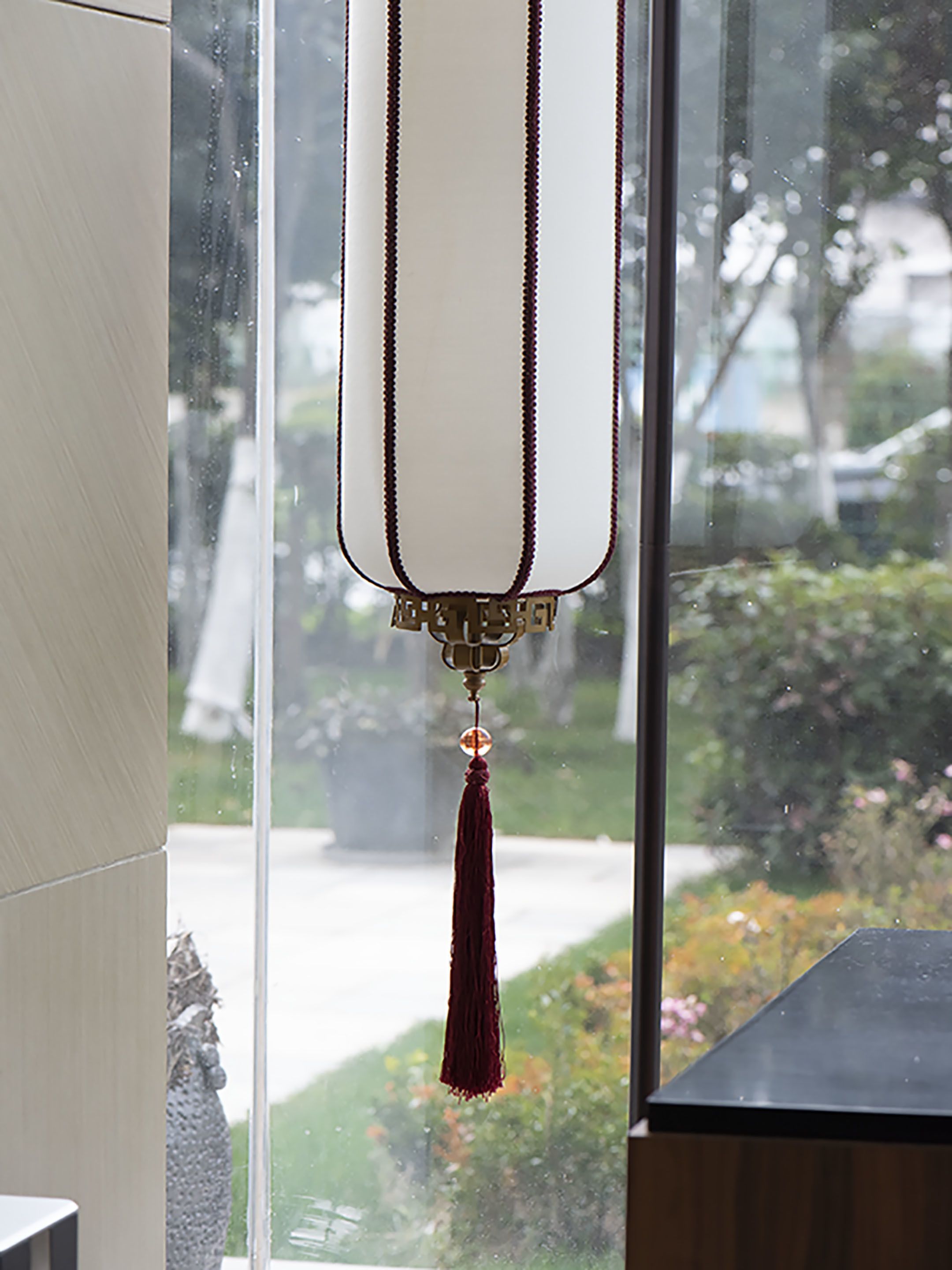 A hanging ornament with a tassel, a window with a view of a garden and parked cars, and a building exterior.
