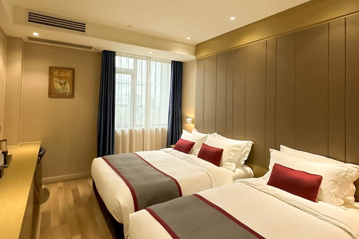 A hotel room with two beds, a desk, and a large window with curtains.