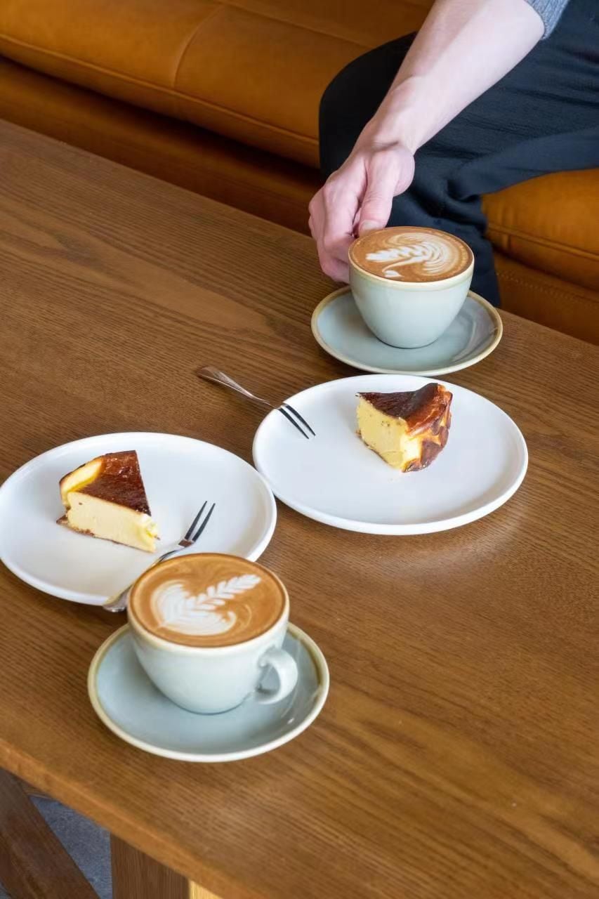 A table with a cup of coffee and two slices of cheesecake on plates.