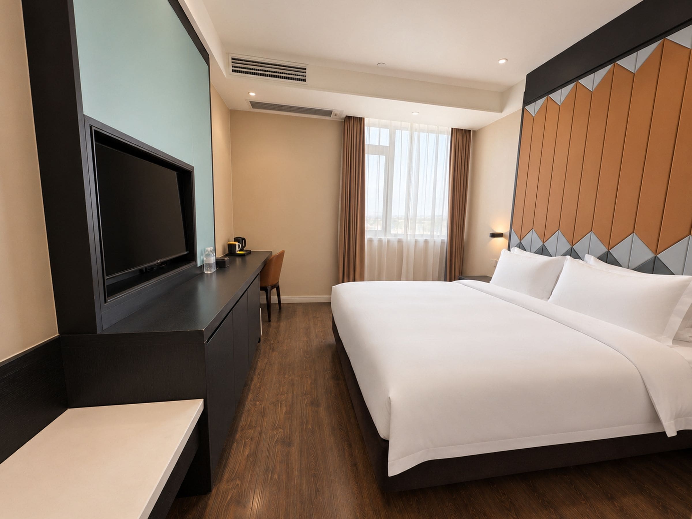 A hotel room with a bed, a desk, a television, and a window with curtains.