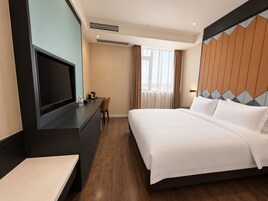 A hotel room with a bed, a desk, a television, and a window with curtains.