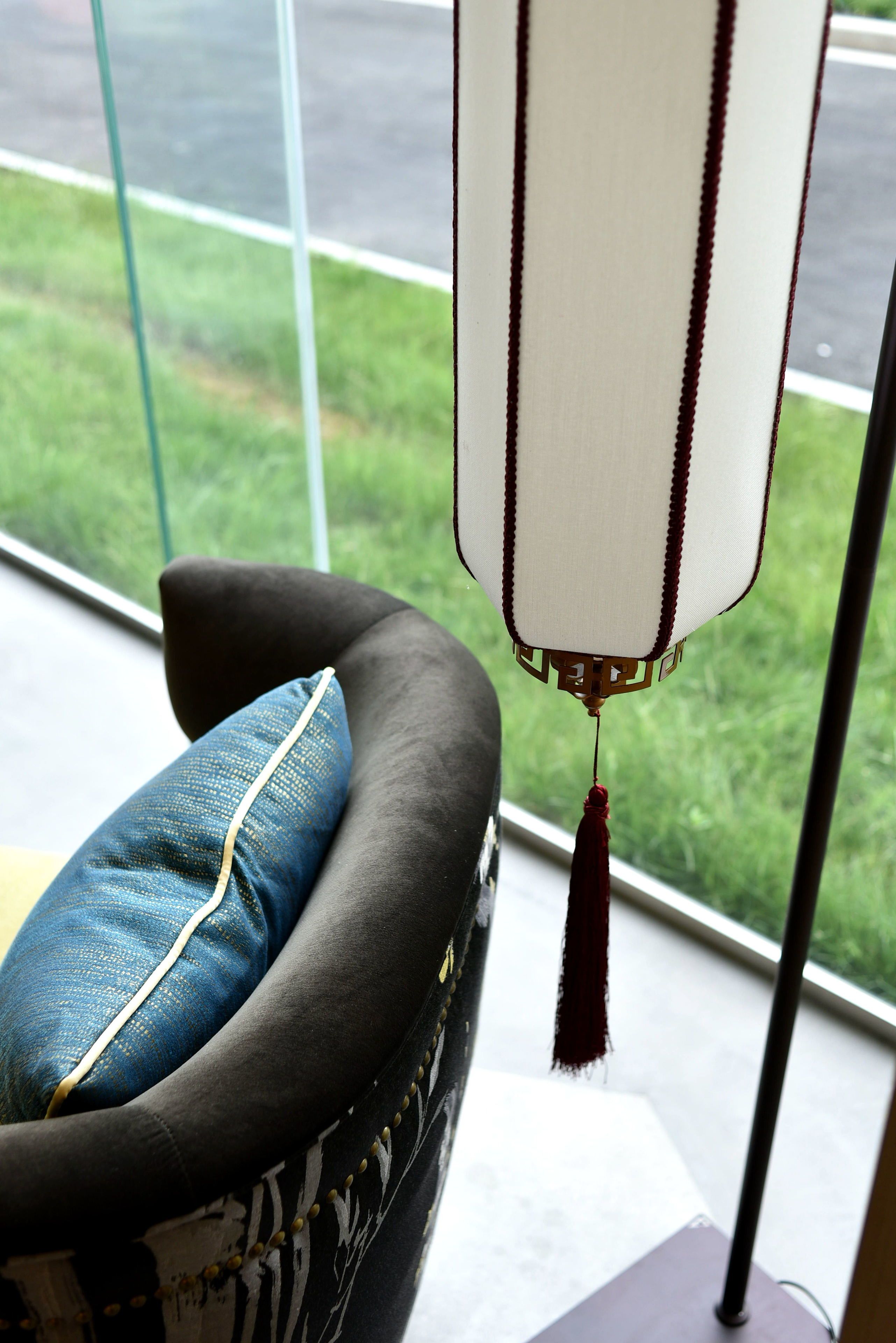 A room with a view of a grassy area through a window, a black sofa with a blue pillow, and a hanging decorative item.