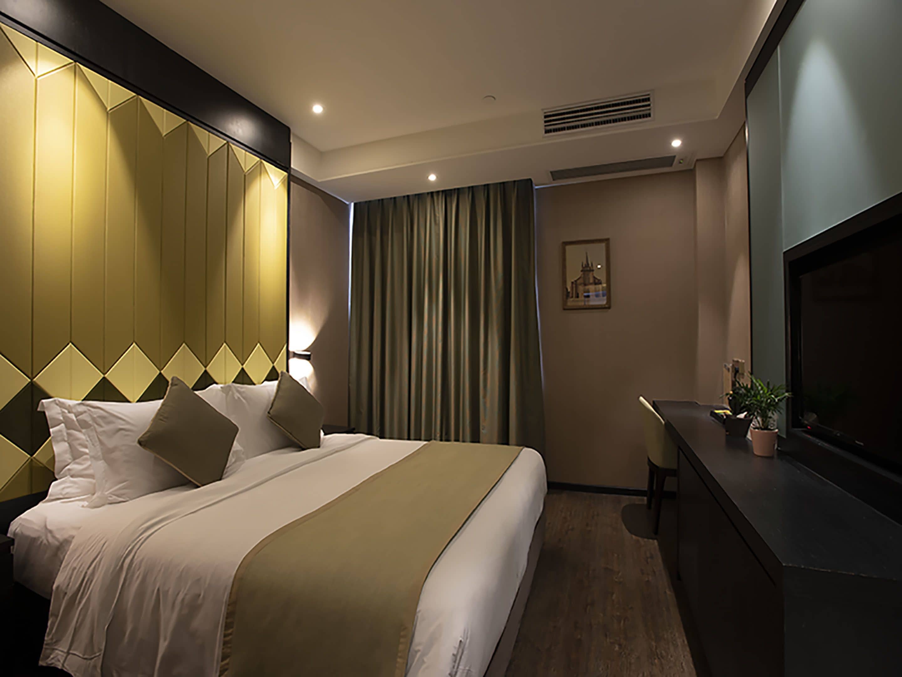 Habitación de hotel con una cama grande, un escritorio, un televisor y una ventana con cortinas.