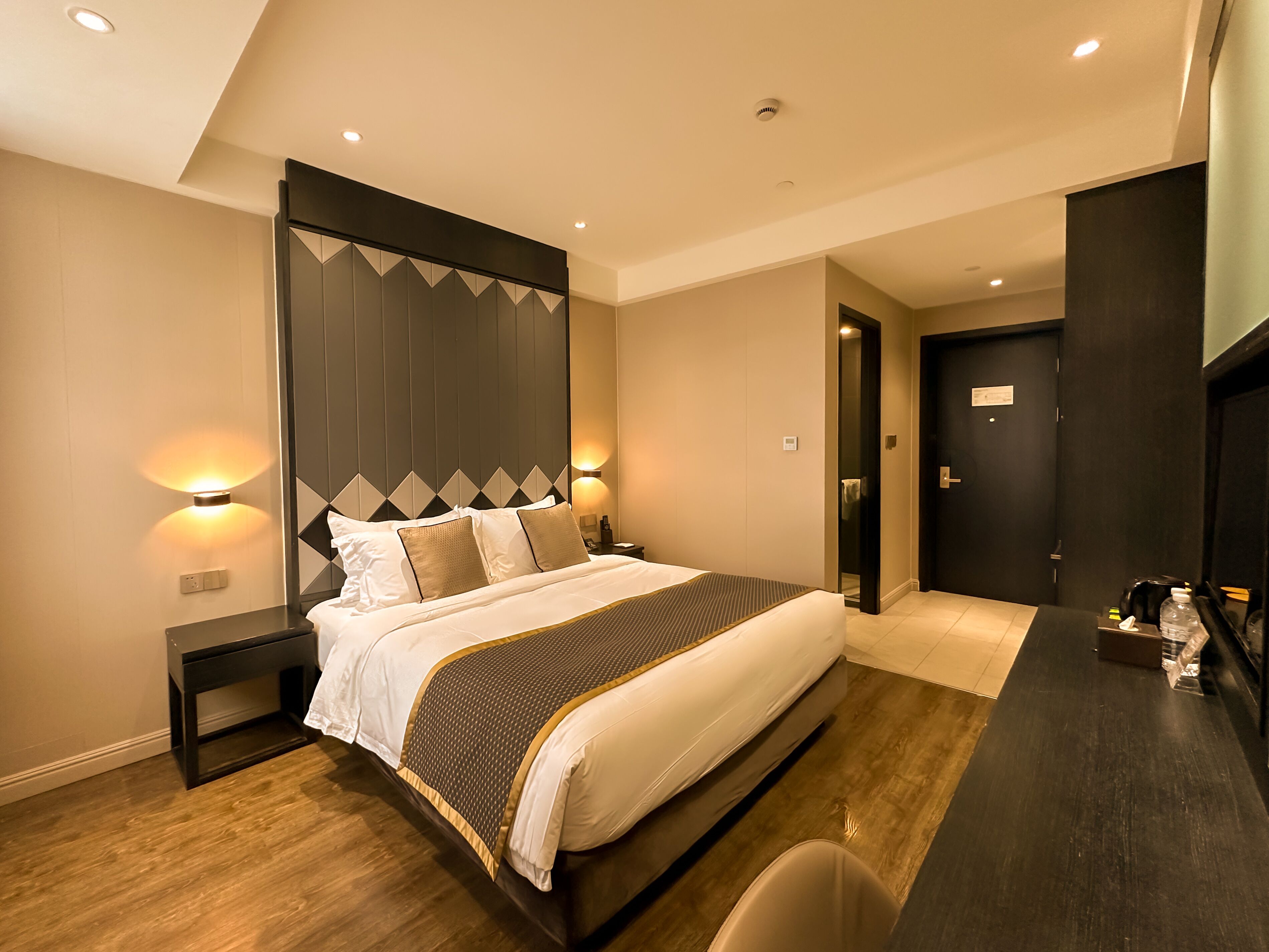 A modern hotel room with a large bed, bedside tables, a desk, and a wardrobe.