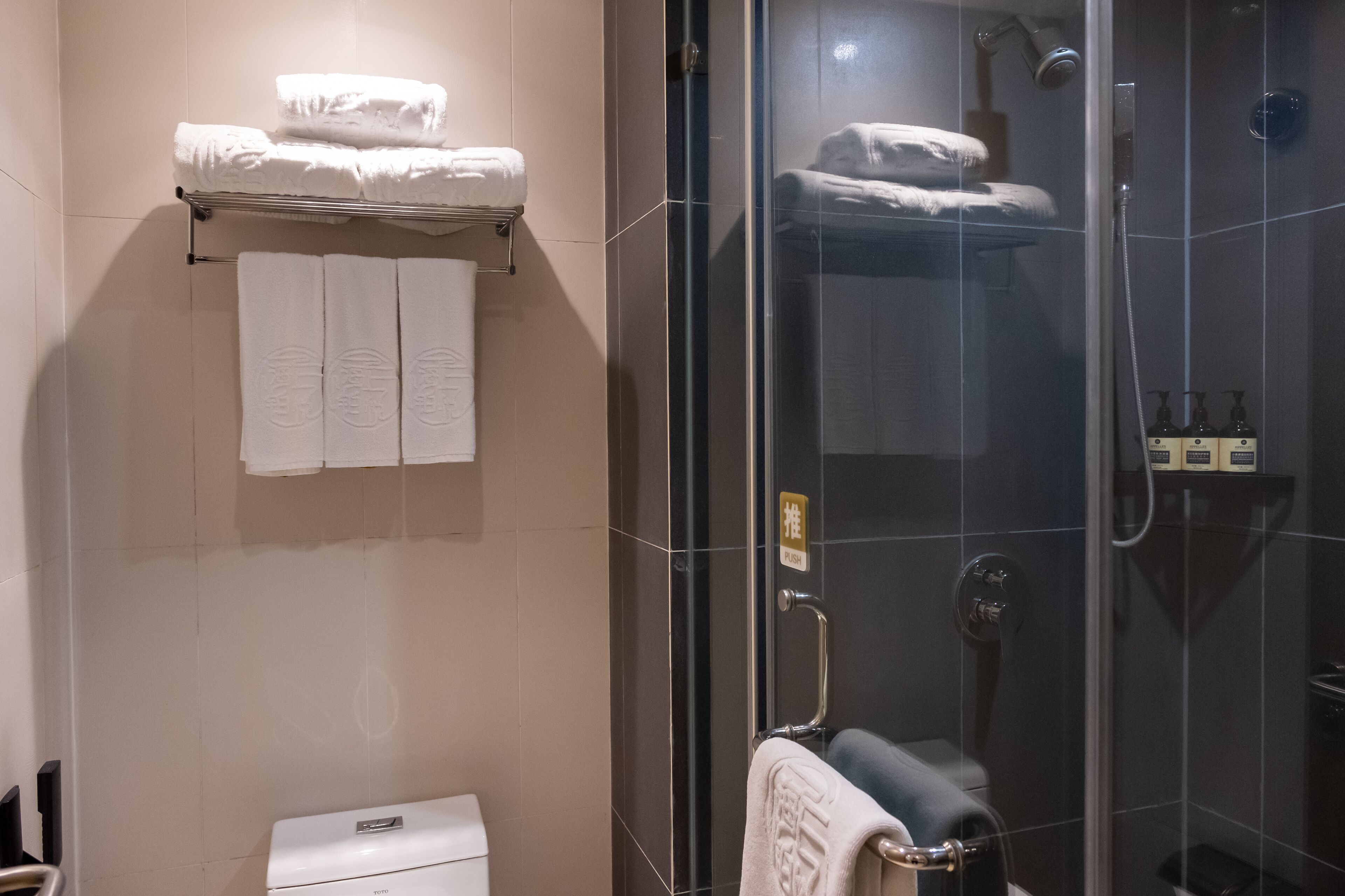 A modern bathroom with a glass shower enclosure, a toilet, and a towel rack with folded towels.