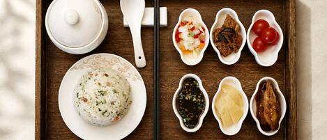 A wooden tray with a bowl of rice, a spoon, and various small dishes containing different foods.