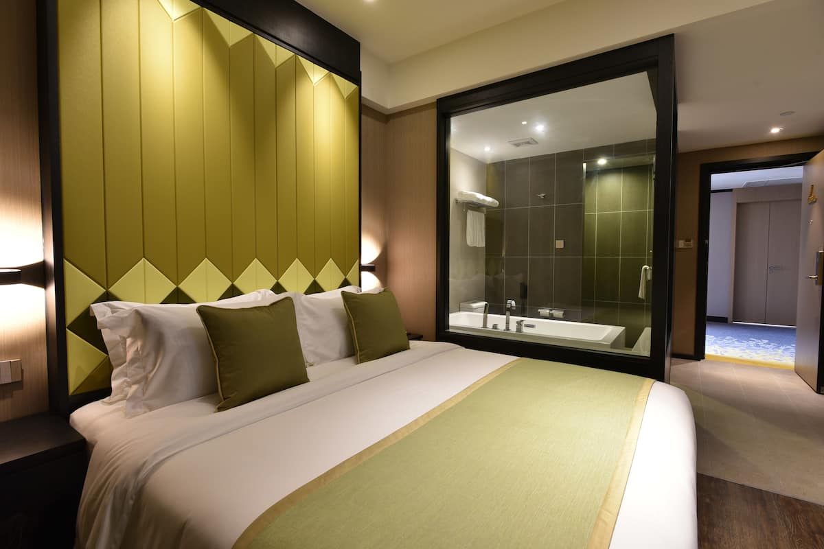 A hotel room with a large bed, a glass-enclosed shower, and a view of the hallway.