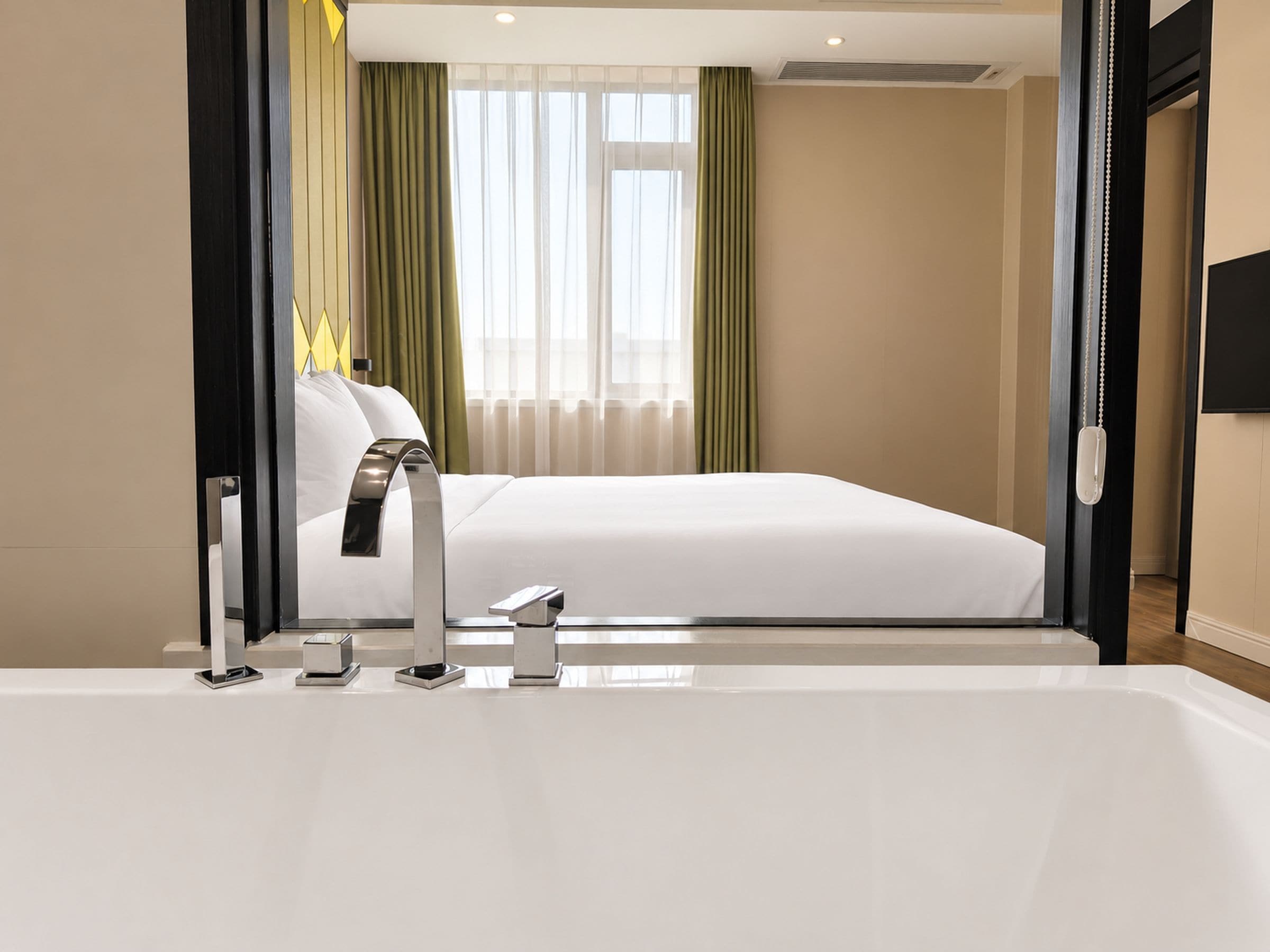 Una camera d'albergo moderna con un letto grande, un bagno con vasca e vista sulla città dalla finestra.