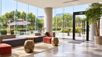 Una hall moderna con ampie vetrate, zone relax e una colonna centrale.