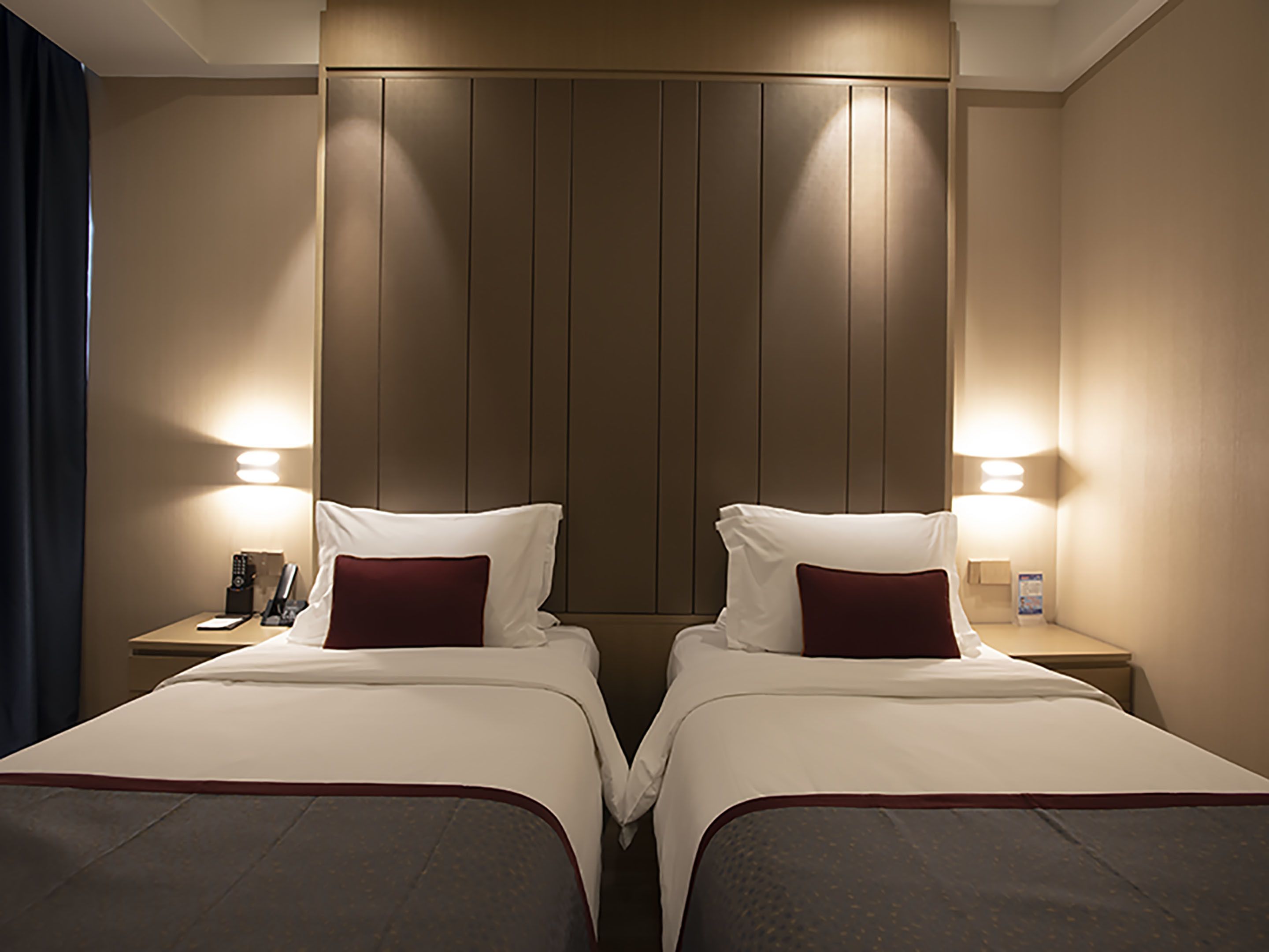 A hotel room with two beds, each with a pillow and a bedside table with a lamp.