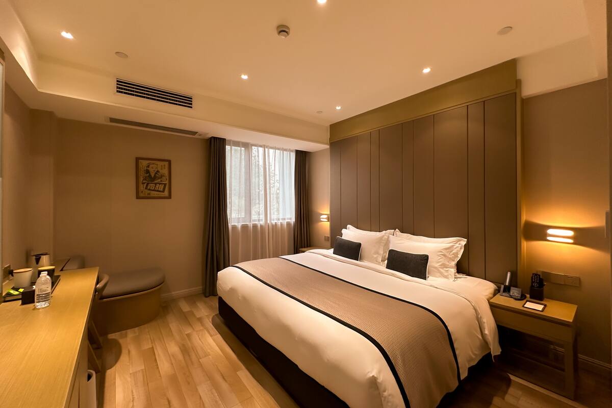 A hotel room with a large bed, bedside tables, a desk, and a window with curtains.